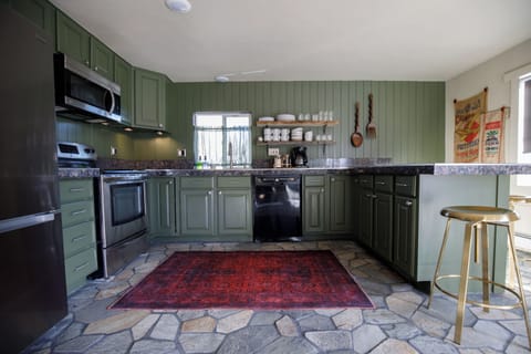 - Cook up cabin style feasts in this earthy green kitchen with stone floors and open shelving
- Fully stocked with stainless appliances, dishware, and a cozy coffee corner
- Warm wood accents and café style touches create a welcoming alpine vibe
