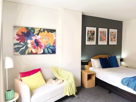 Relax and unwind in our charming bedroom retreat. You'll find a supremely comfortable bed with soft pillows, a cozy small sofa perfect for reading or lounging, and warm, inviting light from the bedside lamps. 