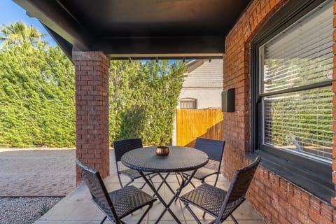 Covered brick patio with a bistro table for four—an easy spot to sip coffee in the shade, catch up over snacks, or wind down outside with a candle flicker on the tabletop.