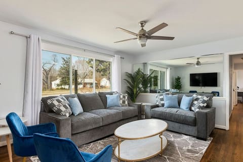 Step into a living room that blends elegance and comfort, with stylish blue chairs and a refreshing ceiling fan with TV