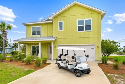 Bright coastal home featuring convenient golf cart access and tropical landscaping in a peaceful neighborhood setting.