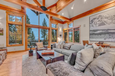 Living Room: L-shaped couch, chair with/ottoman, club chair, chess table w/2 chairs, 70” Smart TV, wood-burning fireplace, soaring windows with Martis Valley views