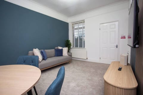 Modern and cozy living space with a stylish blue accent wall, comfortable sofa, dining area, and TV. Bright, inviting, and perfect for relaxation.