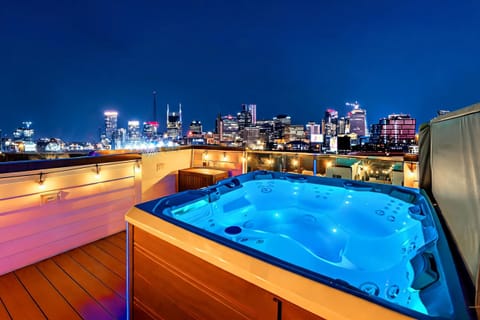 Hot tub on the rooftop, city skyline glowing, string lights overhead. Book your group getaway with Misfit Homes and end every night soaking in views
