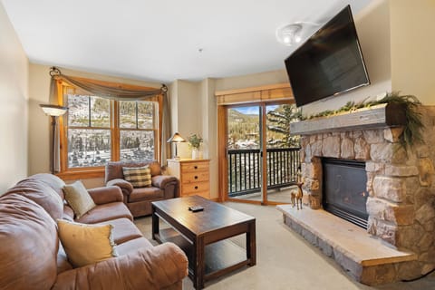 Unwind in your cozy living room featuring a stunning stone fireplace and mountain views through panoramic windows.