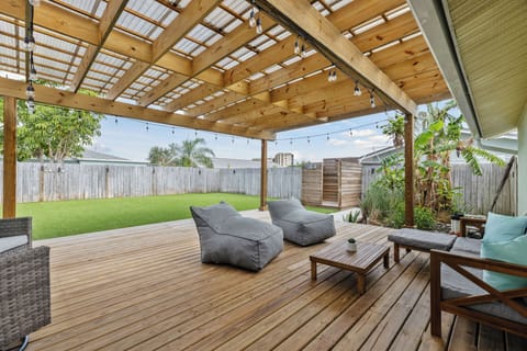A cozy wooden deck with soft seating, greenery & warm lights