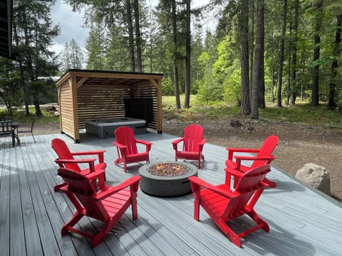 Your own outdoor retreat: 7-person hot tub beneath a covered privacy gazebo, paired with a fire table and Adirondack chairs on a spacious Trex deck.