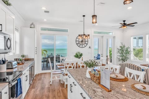 Bright Kitchen + Dining Area | Balcony Access & Water Views Enjoy cooking in this sleek, fully stocked kitchen with easy access to oceanfront dining and drinks outside.