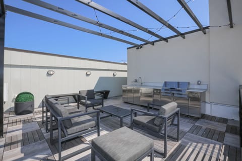 Sunlit rooftop patio w/ lounge seating & dining area, perfect for relaxing under open sky

