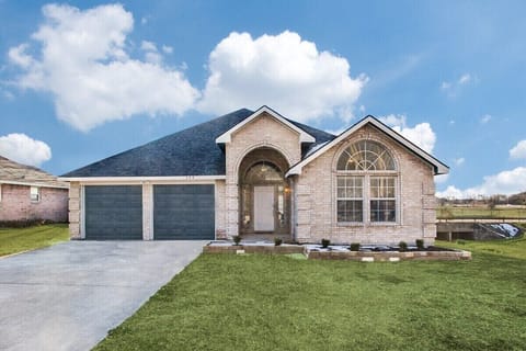 The stone-and-brick facade features an arched entry, broad driveway, three-car garage, and neatly maintained front lawn.