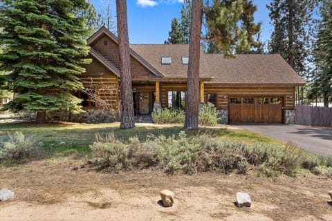 Front exterior with garage door, driveway, front entry, skylights, lawn, shrubs, fence, and tall trees.