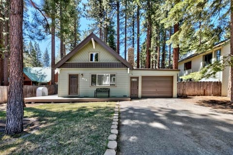 Front exterior with front deck, bench, garage door, driveway, chimney, mailbox, fence, and tall trees.