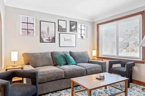 Living room with a gray sofa, two charcoal armchairs, teal pillows, wood coffee table and blue patterned rug beneath a gallery wall.