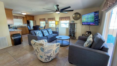 Spacious Coastal Beach House Living Room with Modern Amenities and Large TV
This inviting open-plan living area features plush blue and gray sofas, a striking seashell-patterned armchair, and a sleek coffee table, perfect for relaxation.