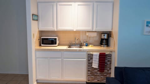 Handy kitchenette with white cabinetry, microwave, sink, and coffee maker—perfect for quick snacks or morning brews. Enjoy practical convenience and coastal charm for guests seeking comfort and ease during their beach stay.