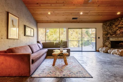 Cozy living room with wood ceilings, large windows, stone fireplace, and warmth.