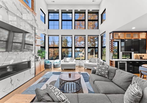 Large sectional in the living room with a wall of windows, two oversized chairs, and a TV. Please note that the electric fireplace is disabled. 