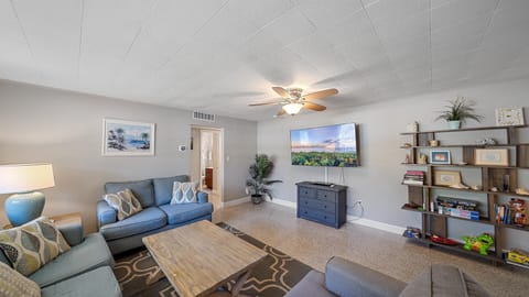 A living room with blue couches, a coffee table, a TV, and a large bookshelf.