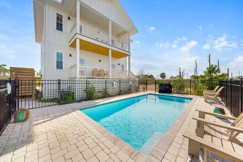 Modern coastal property featuring a private swimming pool with sun loungers and secure fencing in a peaceful residential setting.