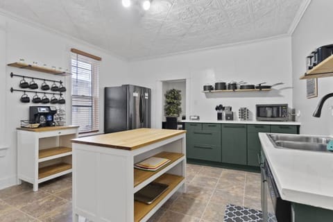 Spacious full kitchen captured from another angle, showcasing a long table, refrigerator, microwave, sink with faucet, drawers underneath, neatly arranged cups, and other essentials—designed for functionality and modern style.