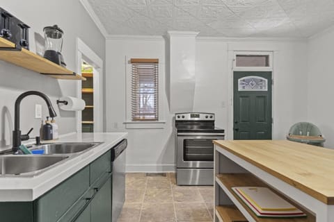 Modern full kitchen featuring a sink with faucet, microwave, stove, door, bright window, sleek flooring, and a cozy table with chairs—designed for functionality and style, offering a welcoming space for cooking and dining
