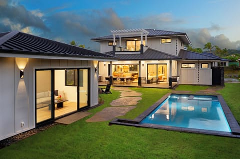 Dusk view of the property showcasing the pool, lush landscaping, and modern architecture.