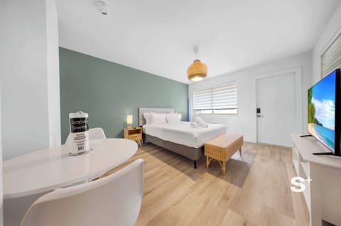 Cozy studio apartment featuring a bed with white linens, a green accent wall, a dining table with chairs, and a TV stand.