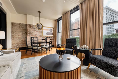 A stylish living and dining space highlighted by exposed brick and natural light from large windows overlooking a bustling cityscape.