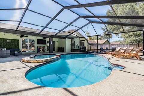 Enjoy a private heated pool and spa under a screened lanai, complete with lounge chairs, a 55" Smart TV, twinkling lights, an ivy wall, and giant Connect Four, perfect for families or groups seeking a fun Clearwater getaway.