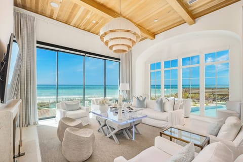 Sink into plush white sofas while gazing at endless ocean views through floor-to-ceiling windows in your elegant beachfront retreat.