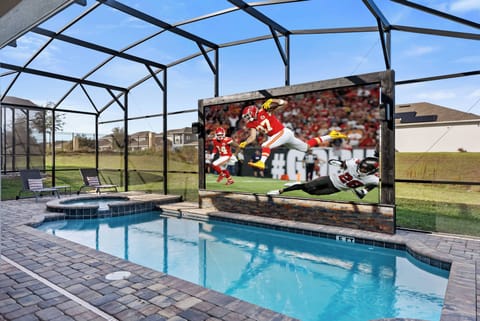 Experience a vibrant setting with a beautiful pool surrounded by elegant pavers and a spacious screened area. Enjoy game day excitement on the large outdoor screen, ideal for relaxing with friends or family under the Florida sun.