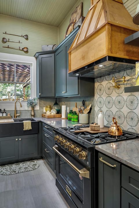Step into a chef’s dream kitchen, where style meets function! This space features a stunning gas range with gold accents, a custom wood range hood, and an eye-catching backsplash. Dark cabinetry, a farmhouse sink, and elegant gold fixtures create a warm and inviting atmosphere. Fully stocked with cookware, utensils, and essentials, it’s ready for your culinary creations!