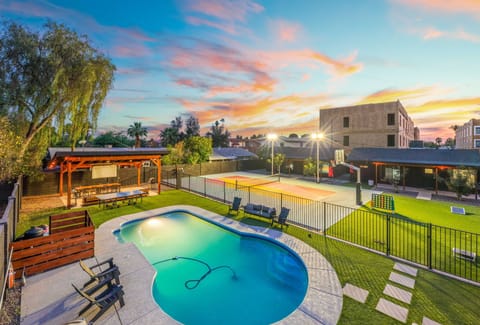 Sunset views over the pool and bright green lawn—start with a refreshing swim, then follow the stepping stones toward the fenced, lit courts for an easy evening game.