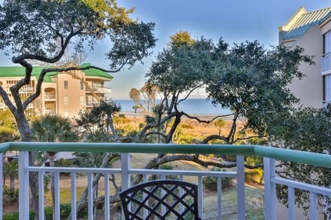 A peaceful, palm-lined landscape unfolds just beyond the balcony, with manicured lawns, winding paths, and mature coastal foliage.