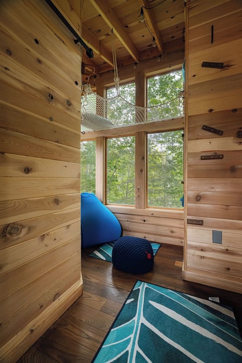Treehouse interior with a beanbag and upper loft net. Climb to the loft net with climbing holds (shoes off please) and feel like you can reach out and touch the trees. Lighting is battery lant