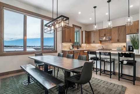 - Dining space with a mix of chairs and bench seating beside a bright kitchen
- Large windows showcase the beauty of the surrounding landscape
- Pendant lights over the island add style and warmth to the open space