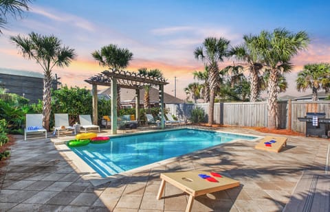 Private backyard oasis with a pool, palm trees, lounge seating, games, and sunset views.