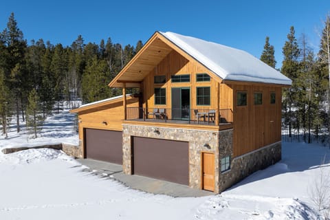 Beautiful mountain chalet with snow-covered roof and stone-wood exterior, nestled among winter evergreens.