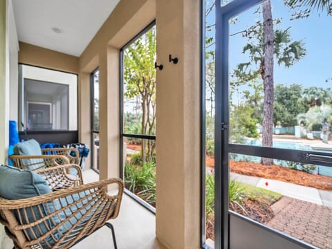Relax in your private screened balcony with wicker seating, enjoying garden views and tropical palms through floor-to-ceiling windows.
