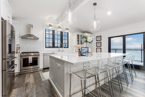 The modern kitchen boasts a large island with seating for six, perfect for enjoying a morning coffee or a late-night snack. The sleek appliances, the white cabinetry, and the beautiful waterfront view create a stylish and functional space.