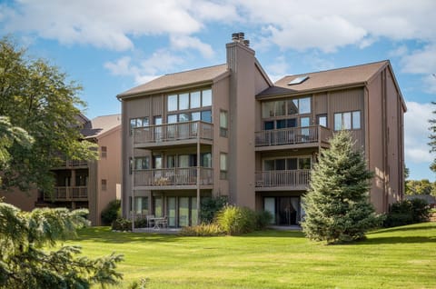 Charming condo exterior set against lush green lawns & mature trees under open blue skies