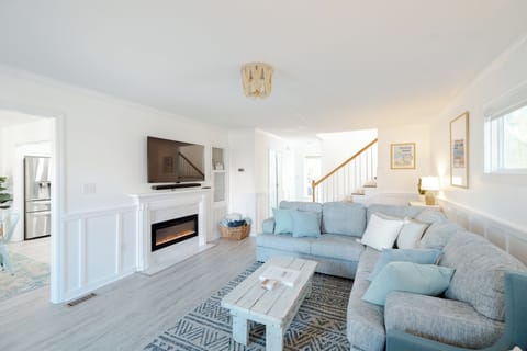 Bright and inviting living room featuring an electric fireplace, plush seating, blackout curtains, and coastal décor.