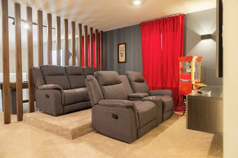 Enjoy a cozy nook with plush gray recliners perfect for movie nights, accented by vibrant red curtains. The unique wooden slats offer an inviting separation, adding charm and character to your experience.
