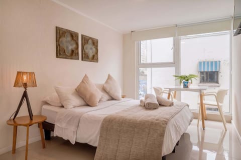 Bright and cozy studio with a comfortable bed and dining area by a large window, perfect for a relaxing stay.