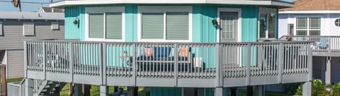 Costa Azul Beach Cottage welcomes guests with its elevated turquoise exterior and spacious wraparound deck in a charming coastal neighborhood.