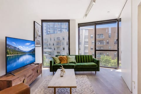 Cozy living room with a green sofa, large TV, and a city view.
