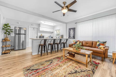 Open living area with a leather sofa, colorful rug, and kitchen bar seating for four.