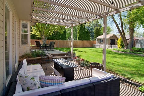 Relax on the large covered patio with a fire pit and cafe lights in the backyard, overlooking a spacious grassy area—perfect for lawn games and enjoying the outdoors. 