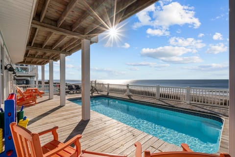 Covered deck with white railings and bright orange Adirondack chairs facing the ocean, dunes below, and wide beach shoreline.