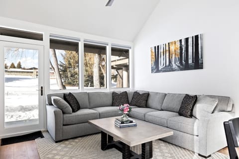- Bright living room with modern gray sectional and chic forest art  
- Floor to ceiling windows showcase snowy scenery outside  
- Inviting space for lounging, conversations, and peaceful moments